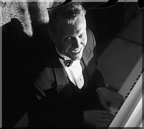 Photo looking down from above at Jerry Michelsen at a grand piano in a tuxedo, smiling