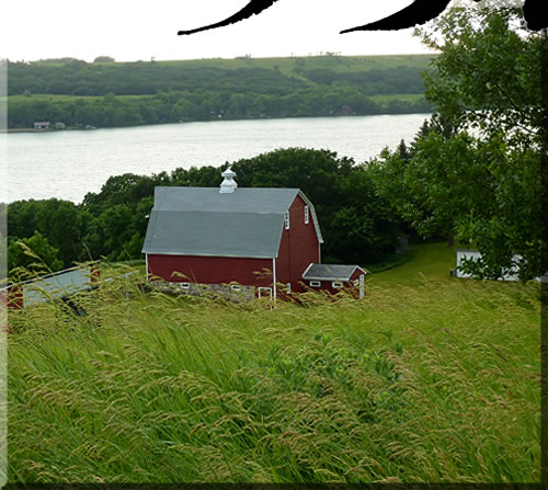 Photo of part of the Michelsen family farm in Minnesota. Looking down from the road above to the red barn with Big Stone Lake and the hills of South Dakota in the background.
